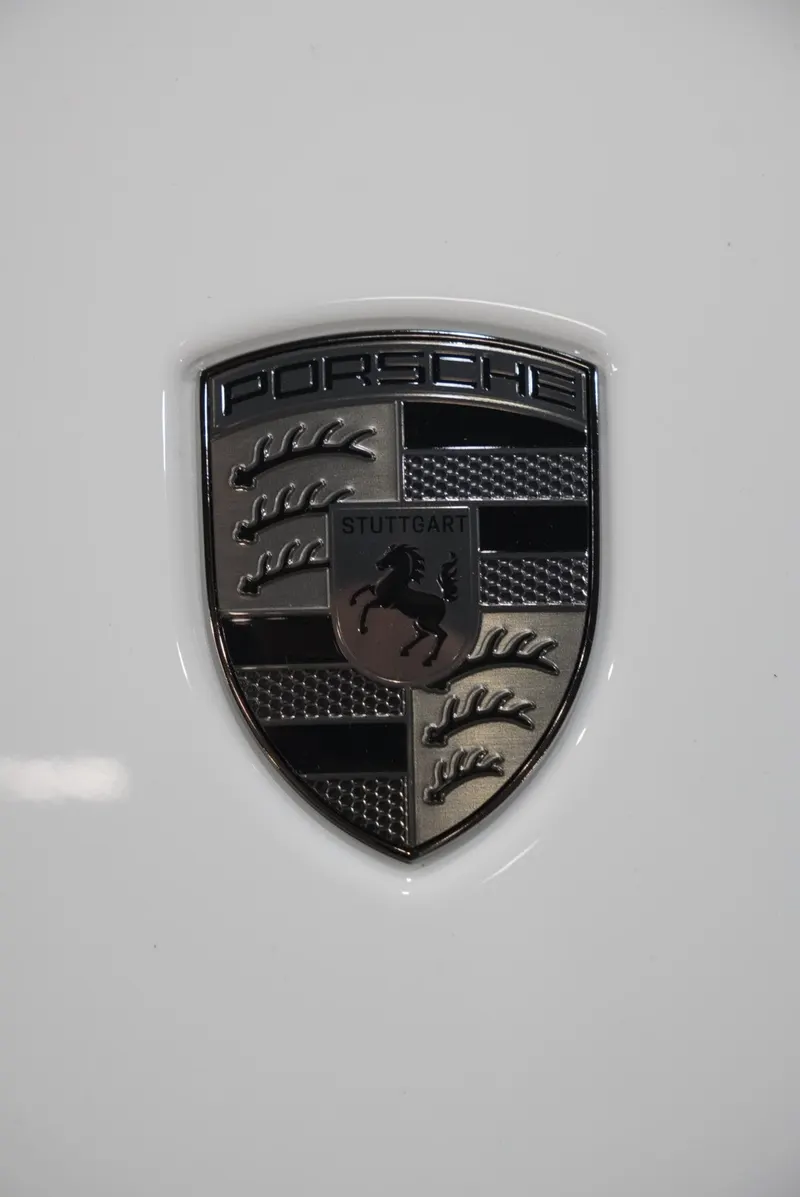 Close-up of a dark-chrome crest emblem on a glossy white hood panel with a soft light reflection.