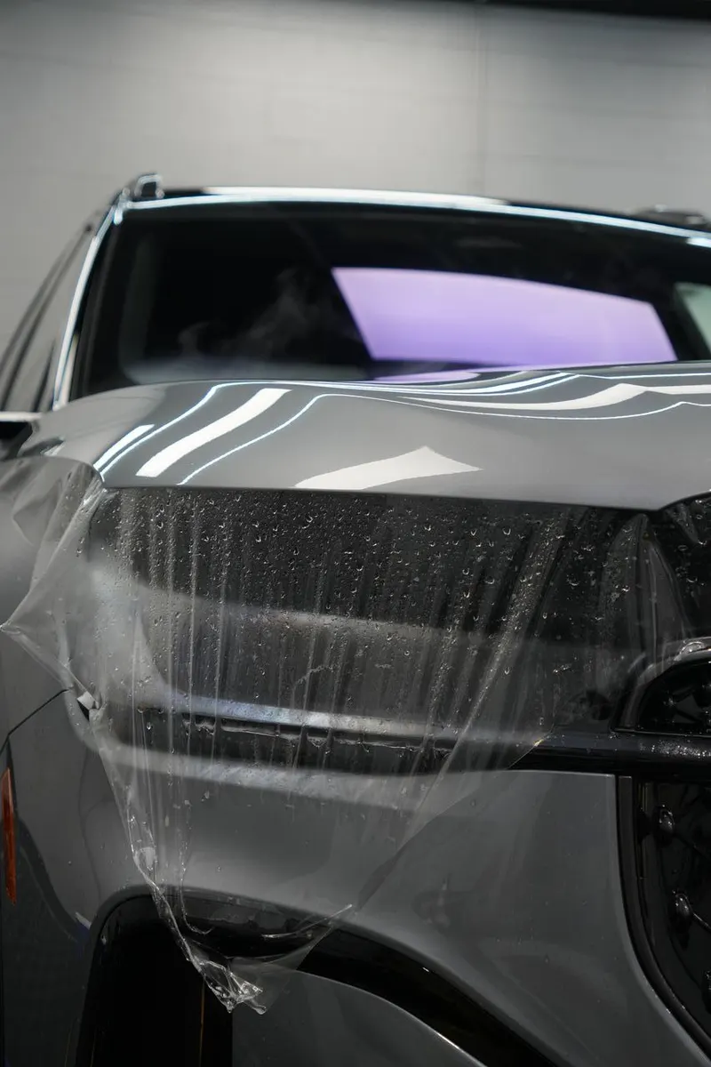 Close-up of a vehicle's rear quarter panel with clear film applied and water droplets on the surface.